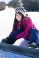 A young woman sitting on a snowboard in the snow.