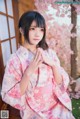 A woman in a pink kimono sitting on a wooden bench.