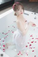 A woman in a white dress sitting in a bathtub with rose petals.