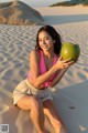 A woman in a pink bikini holding a green coconut.