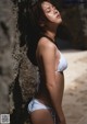 A woman in a white bikini leaning against a rock.