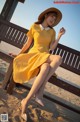 A woman in a yellow dress and hat sitting on a bench.